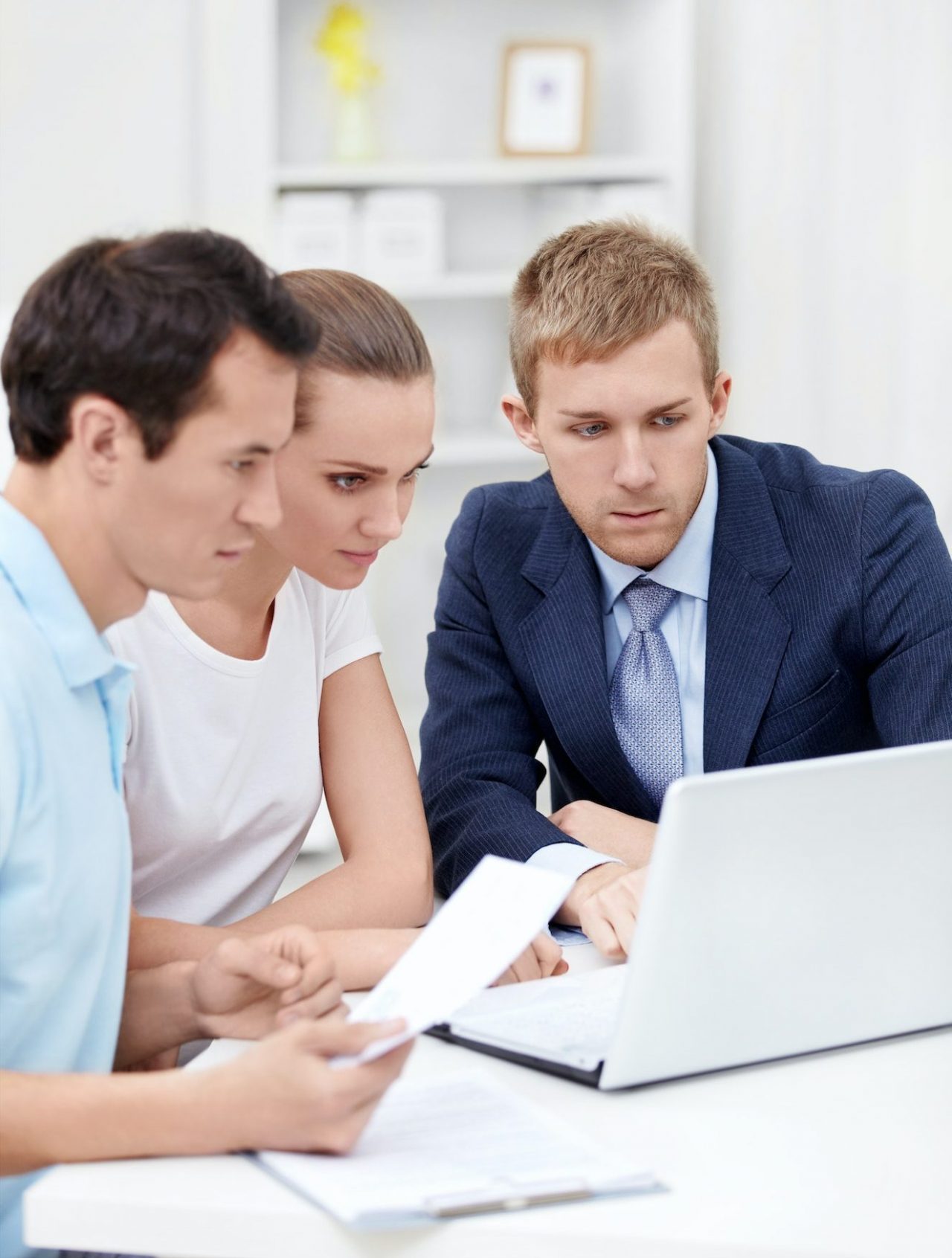 Three professionals, two men and a woman, attentively reviewing documents and working together on a laptop.