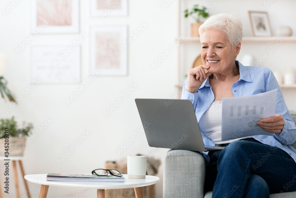 Smiling-senior- woman-reviewing- financial-documents-while-using- a-laptop-at-home- engaged-in-online- financial-planning